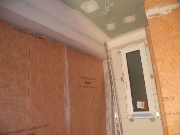 Las paredes del baño impermeabilizadas con la lamina de color naranja y comenzando a alicatar la pared de la ventana